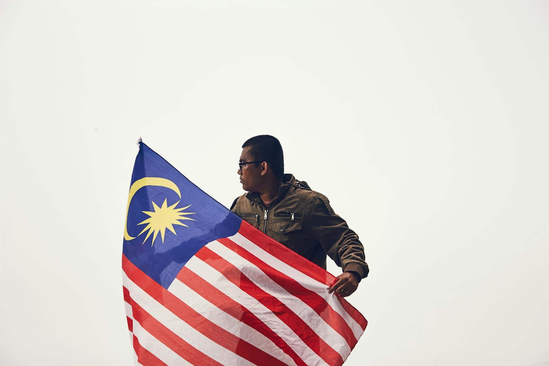 Malaysian man holding the national flag against a plain background.
