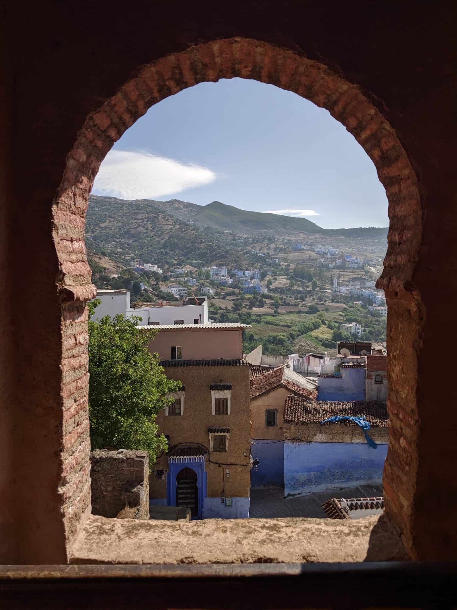 View of Moroccan town and mountains through an arched window.