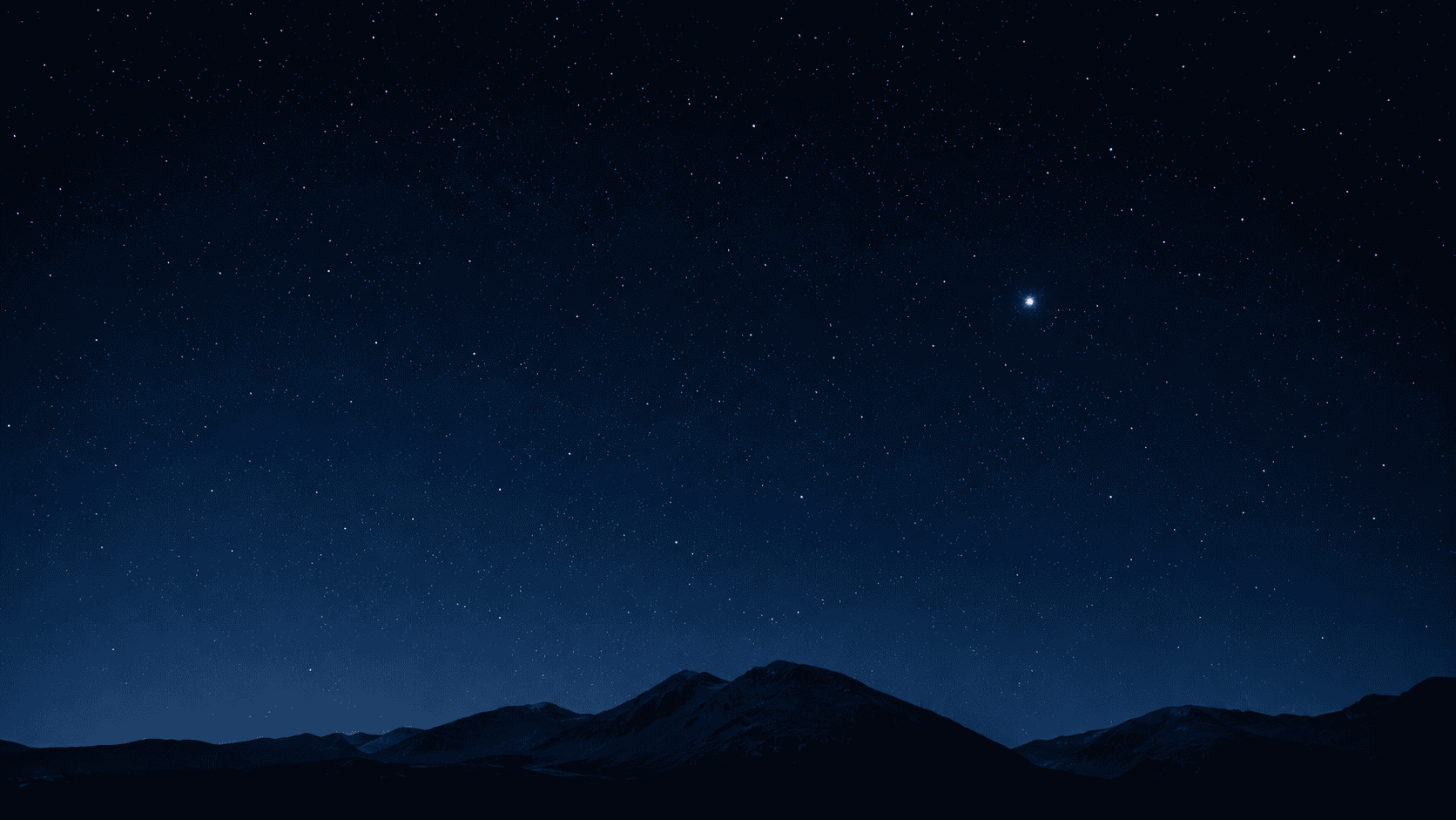 A dark blue night sky filled with stars above a low mountain horizon, with one bright star standing out clearly.